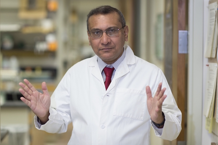 Anindya Duttta, PhD, holds his hands open wide while standing in a white lab coat in his lab.