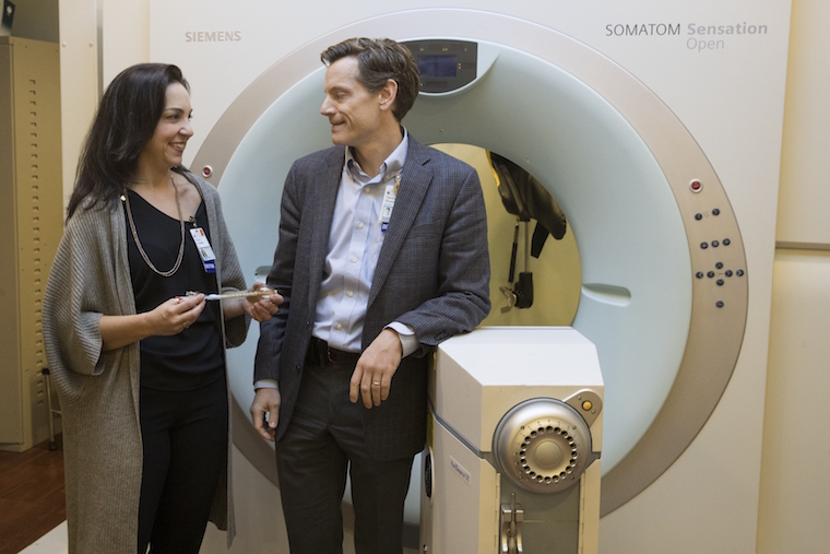 Shayna Showalter, MD, a breast cancer surgeon, and her husband, Tim Showalter, MD, a radiation oncologist, stand in front of a large machine.