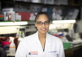 Francine Garrett-Bakelman, MD, PhD, smiles widely while wearing a white lab coat in her lab.