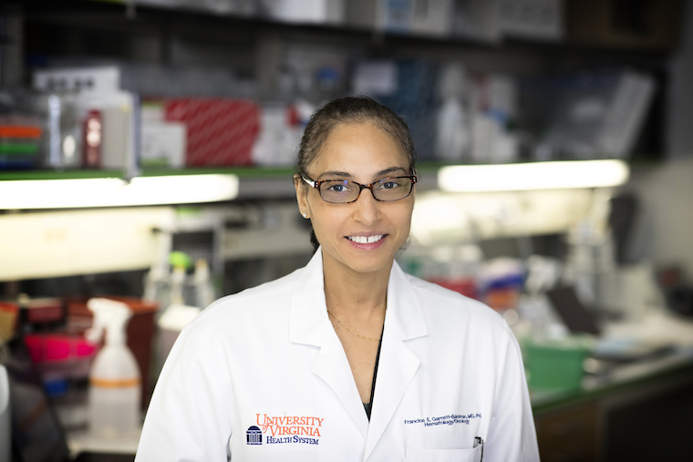 Francine Garrett-Bakelman, MD, PhD, smiles widely while wearing a white lab coat in her lab.