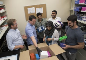 Greg Medlock is joined by the other members of Sean Moore's lab. They are gathered around a cardboard box.