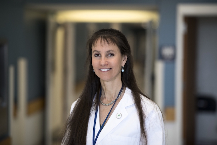 UVA neurologist Karen Johnston, MD, smiles while wearing a white lab coat in front of a blurry hallway.