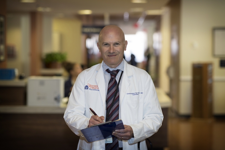 Dr. Christopher M. Kramer holds a clipboard and pen while wearing a white lab coat.