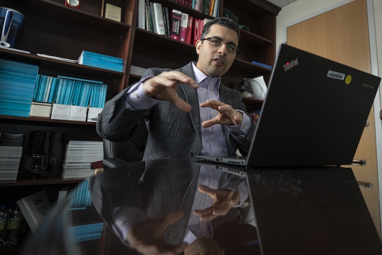 Hessam Sadatsafavi gestures while sitting behind an open laptop.