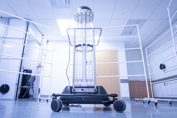 The mask-sanitizing robot. Vertical clear tubes are mounted on a base with wheels.
