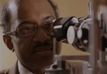 Jayakrishna Ambati looks into a microscope. His face is mostly in shadow.