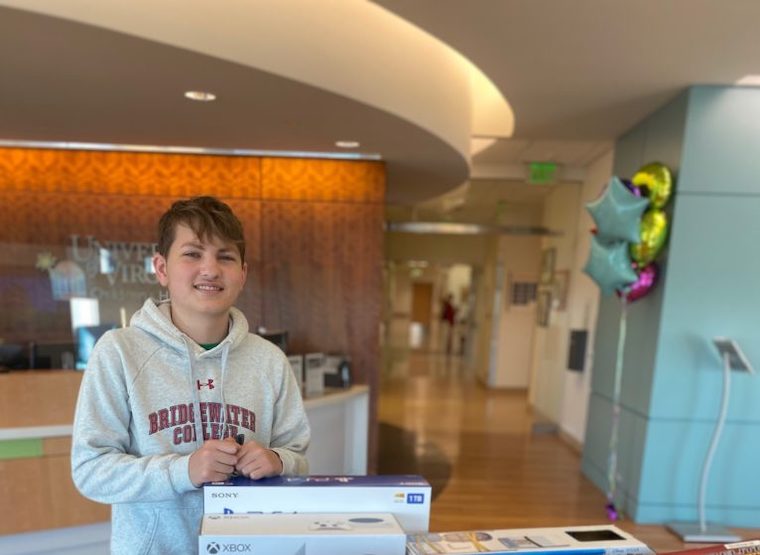 Luke Post stands behind gaming consoles and other activities donated to UVA Children's.