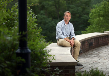 Jochen Zimmer sits on a concrete bench outside his lab. He is surrounded by greenery.