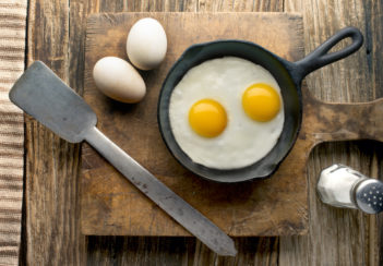 Fried eggs in a cast iron skillet sit on a wooden serving board.