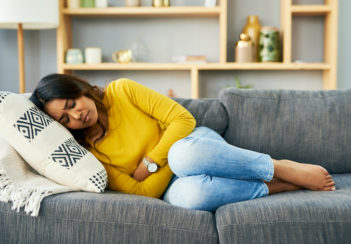 A woman is curled up with premenstrual symptoms on a couch.