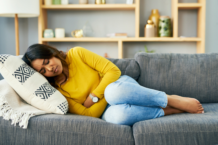 A woman is curled up with premenstrual symptoms on a couch.